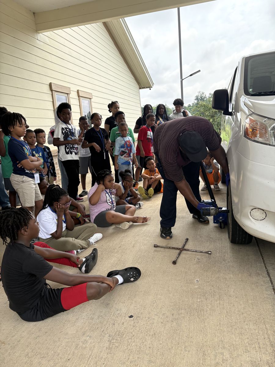 Campers sitting outside the church watching a lesson on changing a tire